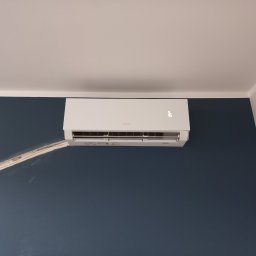 GreenVents KONRAD KOŹBIAŁ - Biały klimatyzator Sinclair na granatowej ścianie, widoczne kable w białej listwie. Minimalistyczny design, temperatura 16 stopni Celsjusza.