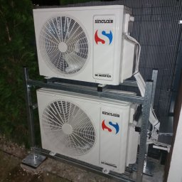GreenVents KONRAD KOŹBIAŁ - Dwa klimatyzatory Sinclair DC Inverter zamontowane jeden nad drugim na metalowej konstrukcji, widoczne przewody i elementy montażowe, tło stanowi ciemna zieleń i szara siatka.