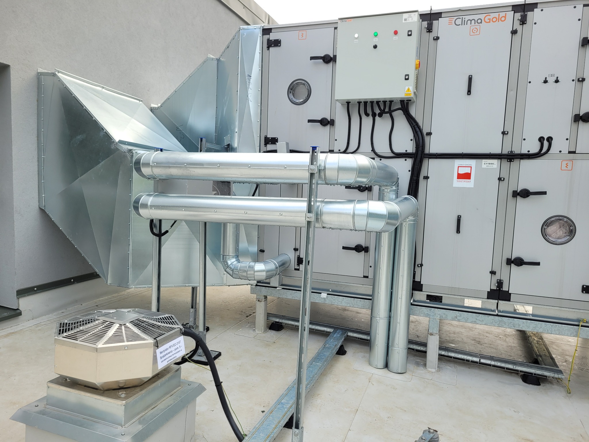 Kompletna instalacja wentylacyjna ClimaGold na dachu budynku, z widocznymi kanałami, rurami i wentylatorem. Szara kolorystyka, nowoczesny design.