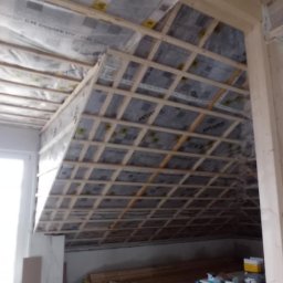 MIL-BUD SYLWESTER CHOMICZ - Poddasze w trakcie ocieplania z widoczną konstrukcją drewnianą, folią izolacyjną Isover i materiałami budowlanymi. Prace ociepleniowe w toku.