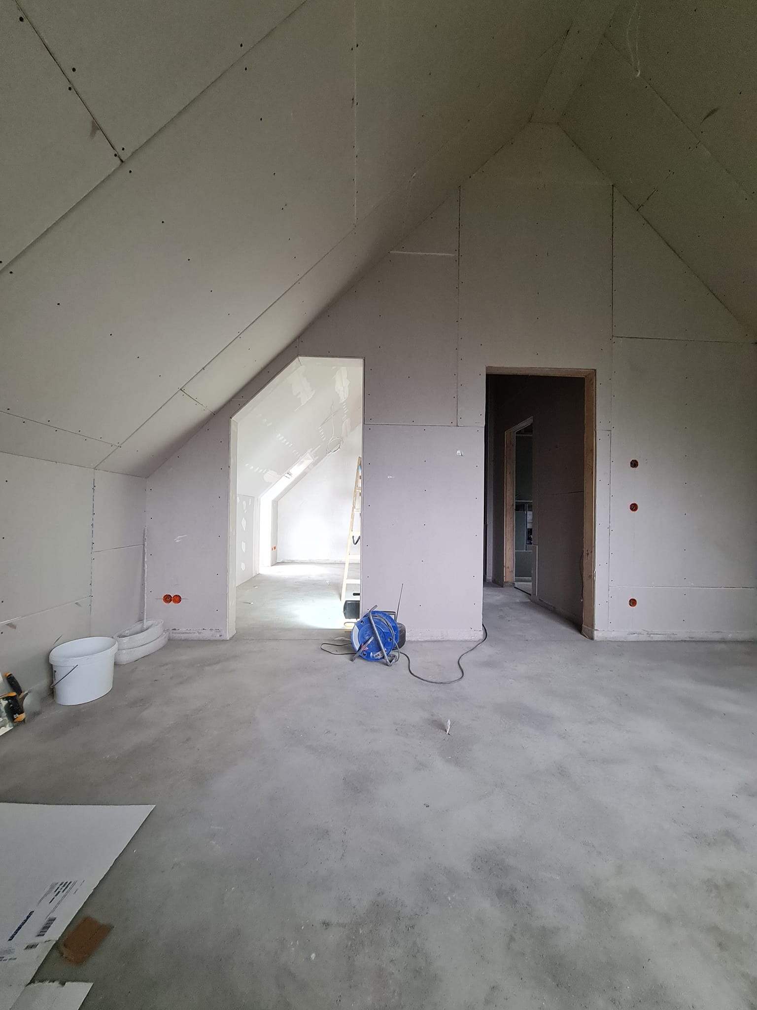 Poddasze z zamontowanymi płytami gipsowo-kartonowymi, widoczne otwory na instalacje elektryczne i narzędzia. Stan surowy przed dalszymi pracami wykończeniowymi.