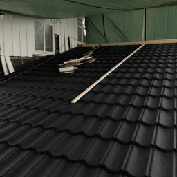 PERRY-BUD Patryk Ślusarski - Czarny dach z blachodachówki modułowej w trakcie montażu, widoczne elementy konstrukcyjne i resztki materiałów, budynek z białym sidingiem w tle.