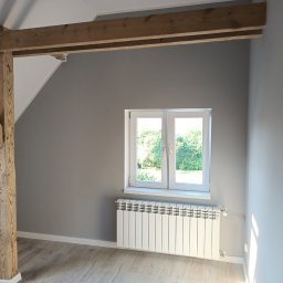 PERRY-BUD Patryk Ślusarski - Szare wnętrze poddasza z drewnianą konstrukcją nośną, białym oknem i grzejnikiem, wykończone panelami podłogowymi.