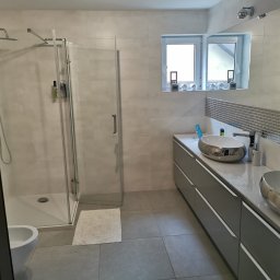 Adrian Orczyk - Nowoczesna łazienka z kabiną prysznicową typu walk-in, podwójną umywalką nablatową w kolorze srebrnym, szarą szafką z szufladami i mozaiką nad blatem.
