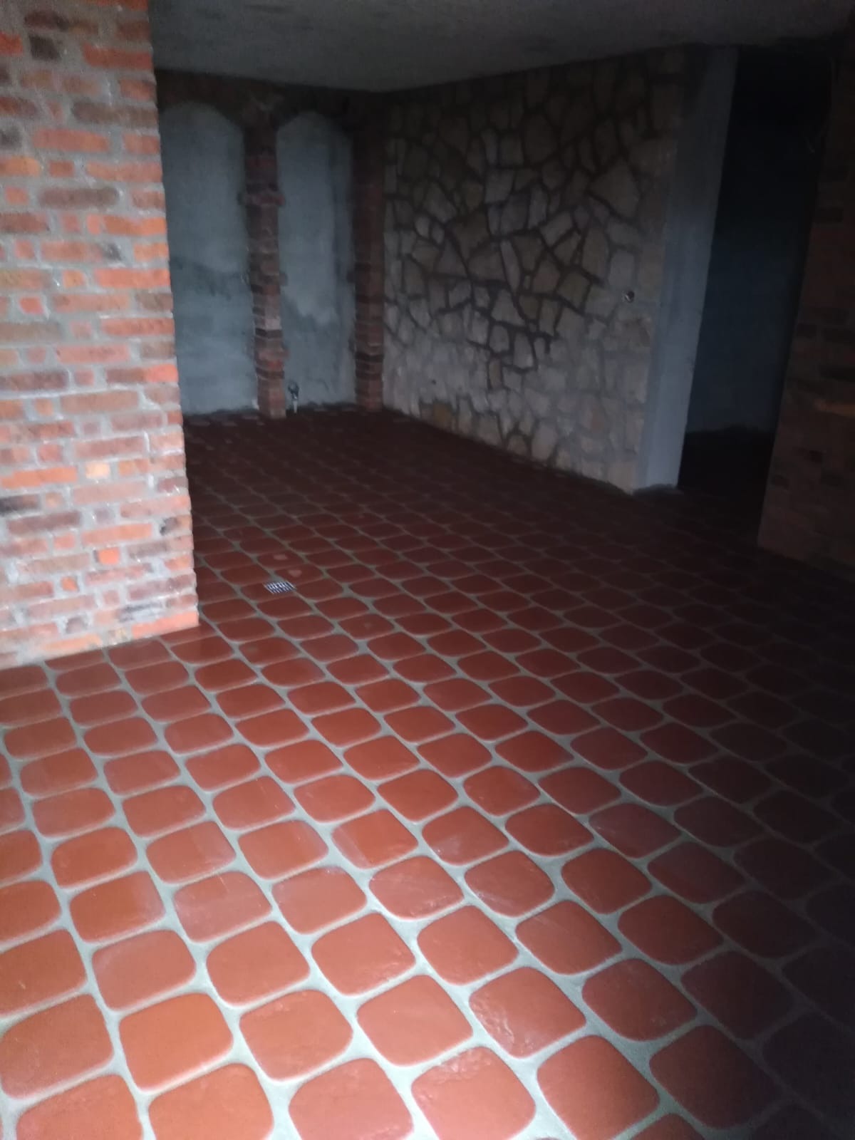 Wykończone wnętrze z czerwoną terakotą na podłodze, ściana z kamienia dekoracyjnego i fragment ściany z czerwonej cegły.