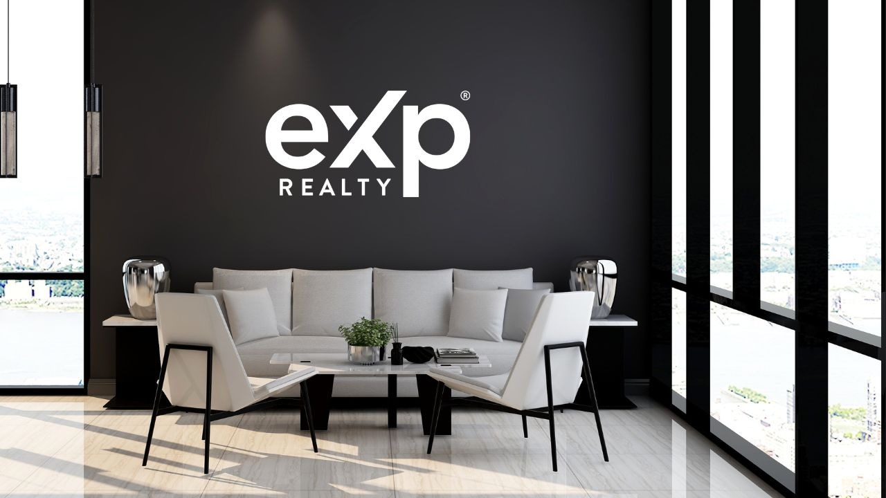 Nowoczesne wnętrze biura agencji nieruchomości: szara sofa, białe krzesła, czarna ściana z logo 'eXp Realty', widok na miasto przez okno.