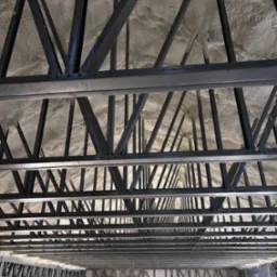 Poddasze z widoczną konstrukcją stalową i zaaplikowaną pianką PUR, tworzącą jednolitą warstwę izolacyjną. Widok z dołu na ocieplony strop.