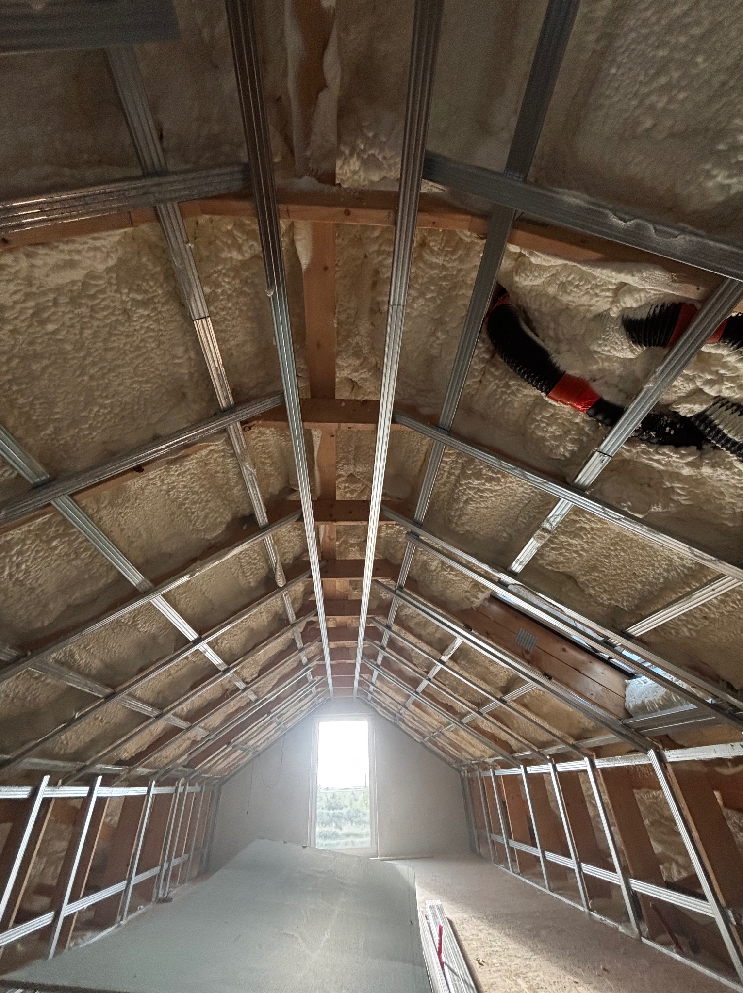 Poddasze z ociepleniem pianką PUR i metalową konstrukcją pod płyty gipsowe, widok z dołu na okno. Ocieplona skośna powierzchnia, widoczne elementy instalacji wentylacyjnej.