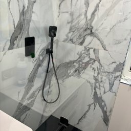 Firma sprzątająca Klaudia Dudek - Nowoczesna kabina prysznicowa z czarną armaturą i białymi płytkami imitującymi marmur, widoczny dozownik mydła w płynie.