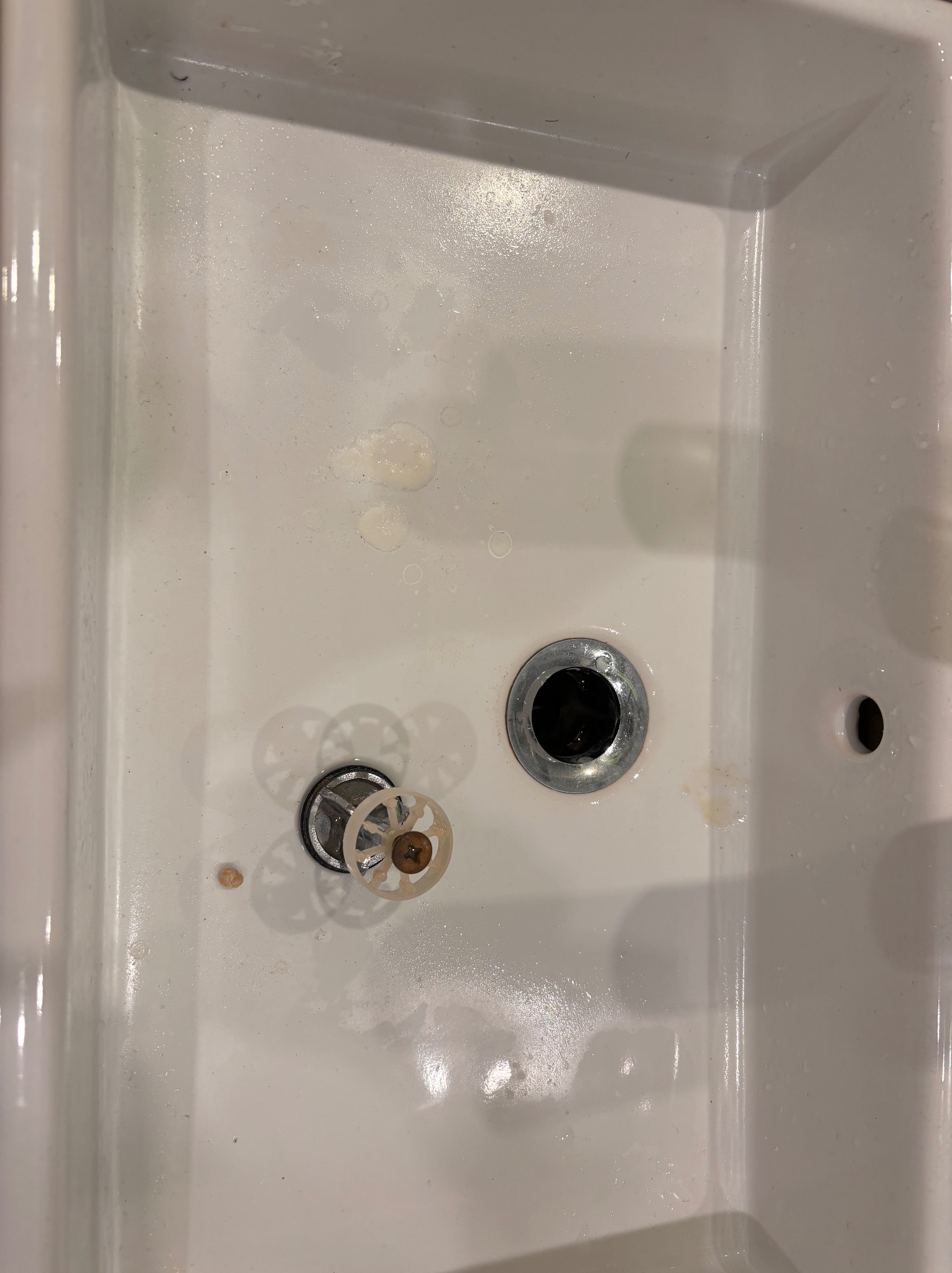 Brudna, biała umywalka z osadem i pozostałościami po mydle, widoczne elementy odpływu i regulatora dopływu wody.