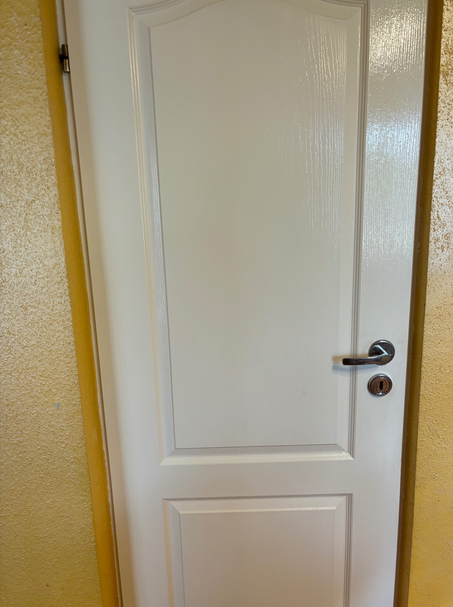 Świeżo pomalowane, białe drzwi wewnętrzne z chromowaną klamką na tle żółtej ściany o wyraźnej fakturze.