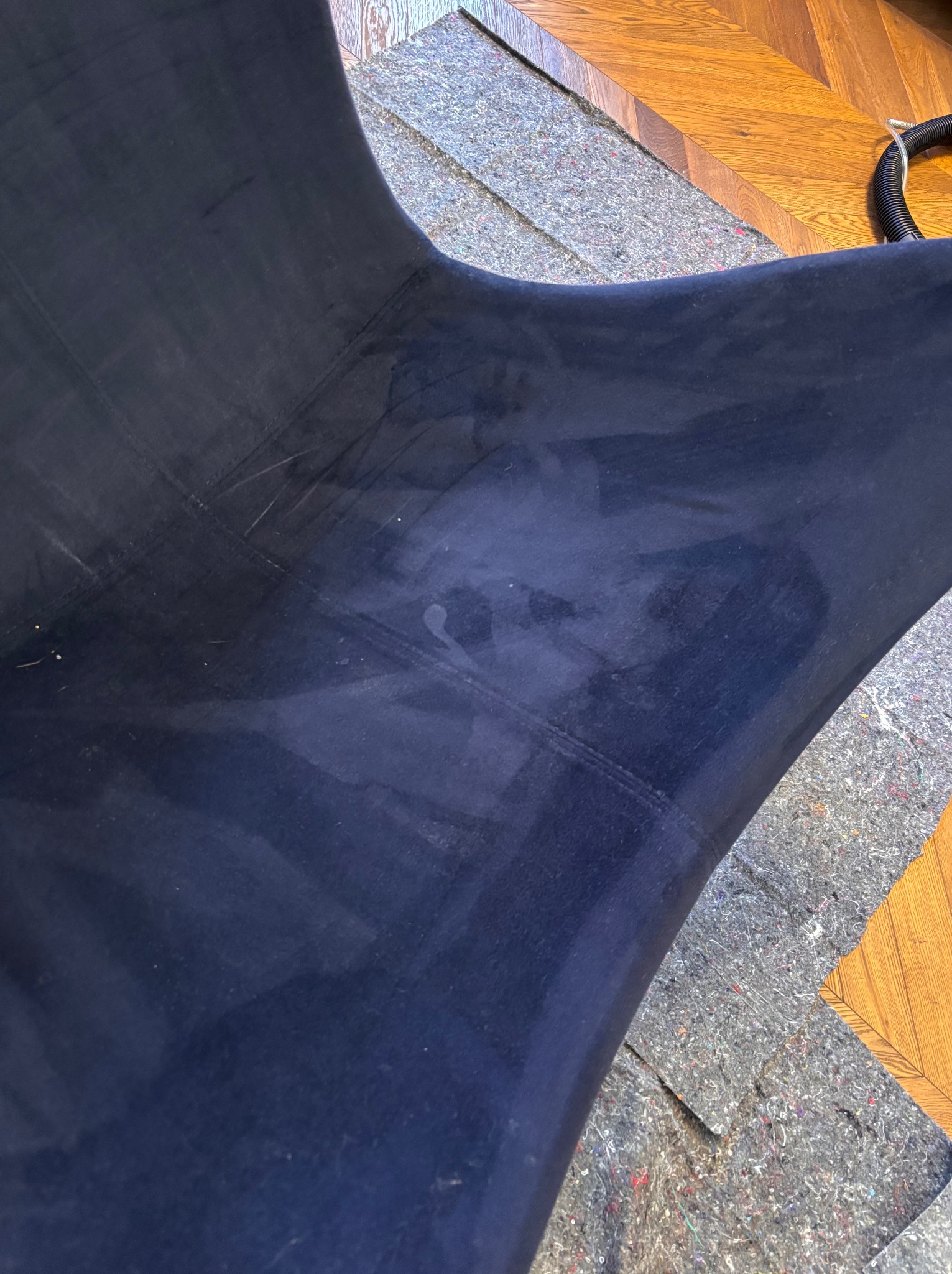 Ciemnoniebieski welurowy fotel z widocznymi plamami po czyszczeniu, otoczony ochronną folią i fragmentem parkietu.