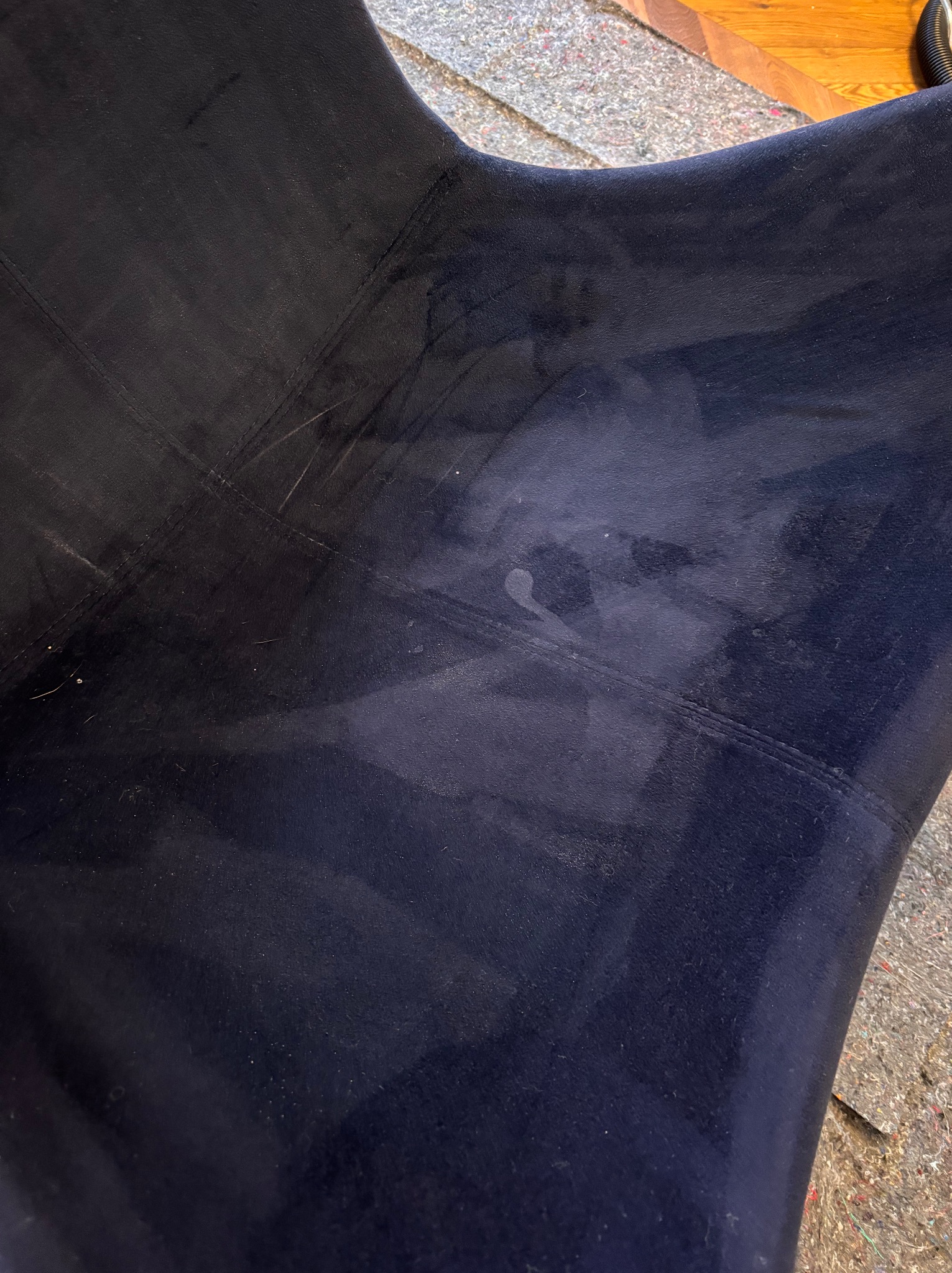 Fragment ciemnoniebieskiego, welurowego fotela z widocznymi plamami po czyszczeniu, szwami i drobnymi zabrudzeniami.
