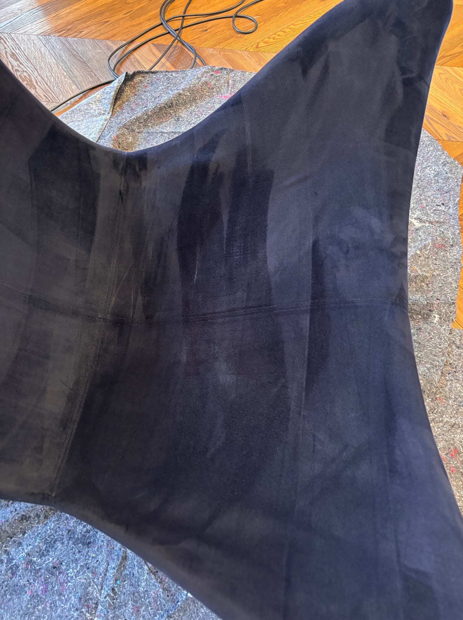 Ciemnoniebieskie welurowe krzesło po czyszczeniu, widoczne jaśniejsze, wilgotne pasy po ekstrakcji zabrudzeń, zabezpieczone filcową matą na drewnianej podłodze.