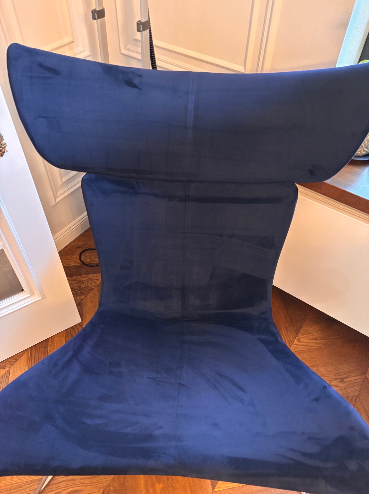 Widok z góry na ciemnoniebieskie, welurowe krzesło o nowoczesnym designie, stojące na parkiecie w jasnym wnętrzu.