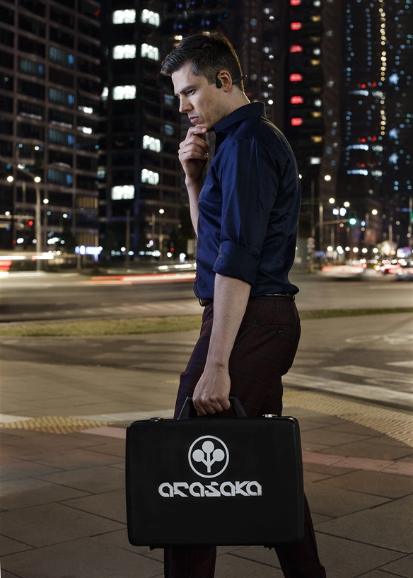Mężczyzna w ciemnej koszuli, z słuchawką w uchu, trzyma czarną aktówkę z logo 'Arasaka' na tle nocnego pejzażu miejskiego z wieżowcami i rozmytymi światłami samochodów.