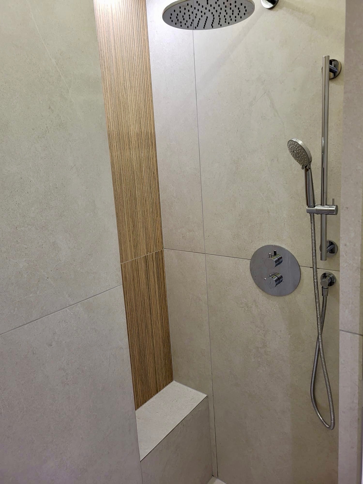 Nowoczesna kabina prysznicowa z deszczownicą i panelami imitującymi drewno. Jasne płytki, minimalistyczna armatura, subtelne oświetlenie.