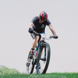 zofia.jpg Zofia Kowalczyk - Zawodnik w kasku na rowerze górskim, numer startowy 204, na zielonej trawie, widok z dołu, niebo w tle, dynamiczne ujęcie.