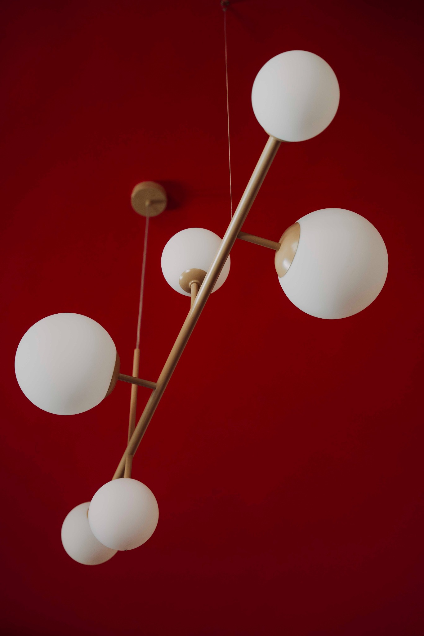 Nowoczesna lampa wisząca z białymi kulami i złotymi ramionami na tle czerwonego sufitu. Minimalistyczny design, oświetlenie wnętrz.