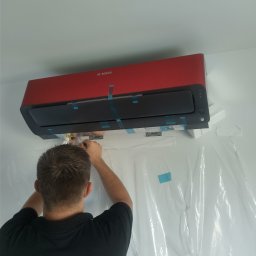 GOWENT SPÓŁKA Z OGRANICZONĄ ODPOWIEDZIALNOŚCIĄ - Monteraż klimatyzatora BOSCH w kolorze czerwonym, zabezpieczonego folią ochronną, podczas podłączania przewodów przez instalatora.