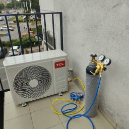 GOWENT SPÓŁKA Z OGRANICZONĄ ODPOWIEDZIALNOŚCIĄ - Biała jednostka zewnętrzna klimatyzacji TCL na balkonie, podłączona do butli z czynnikiem chłodniczym za pomocą żółtych i niebieskich węży oraz manometru.