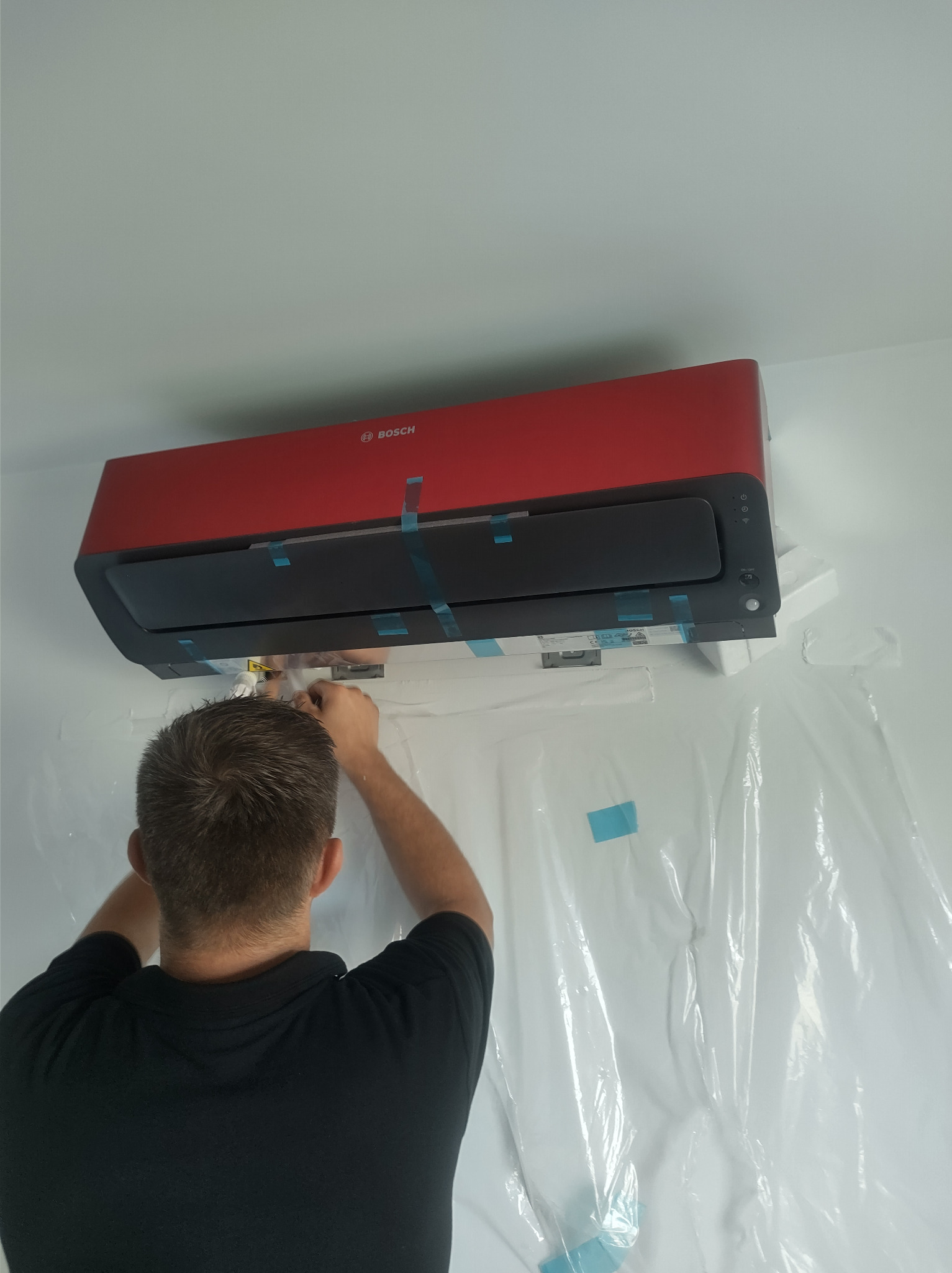 Monteraż klimatyzatora BOSCH w kolorze czerwonym, zabezpieczonego folią ochronną, podczas podłączania przewodów przez instalatora.