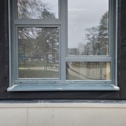 SEBASTIAN GAŃSKI - Szare okno z roletą zewnętrzną w trakcie montażu, widoczne elementy konstrukcyjne i izolacyjne budynku.