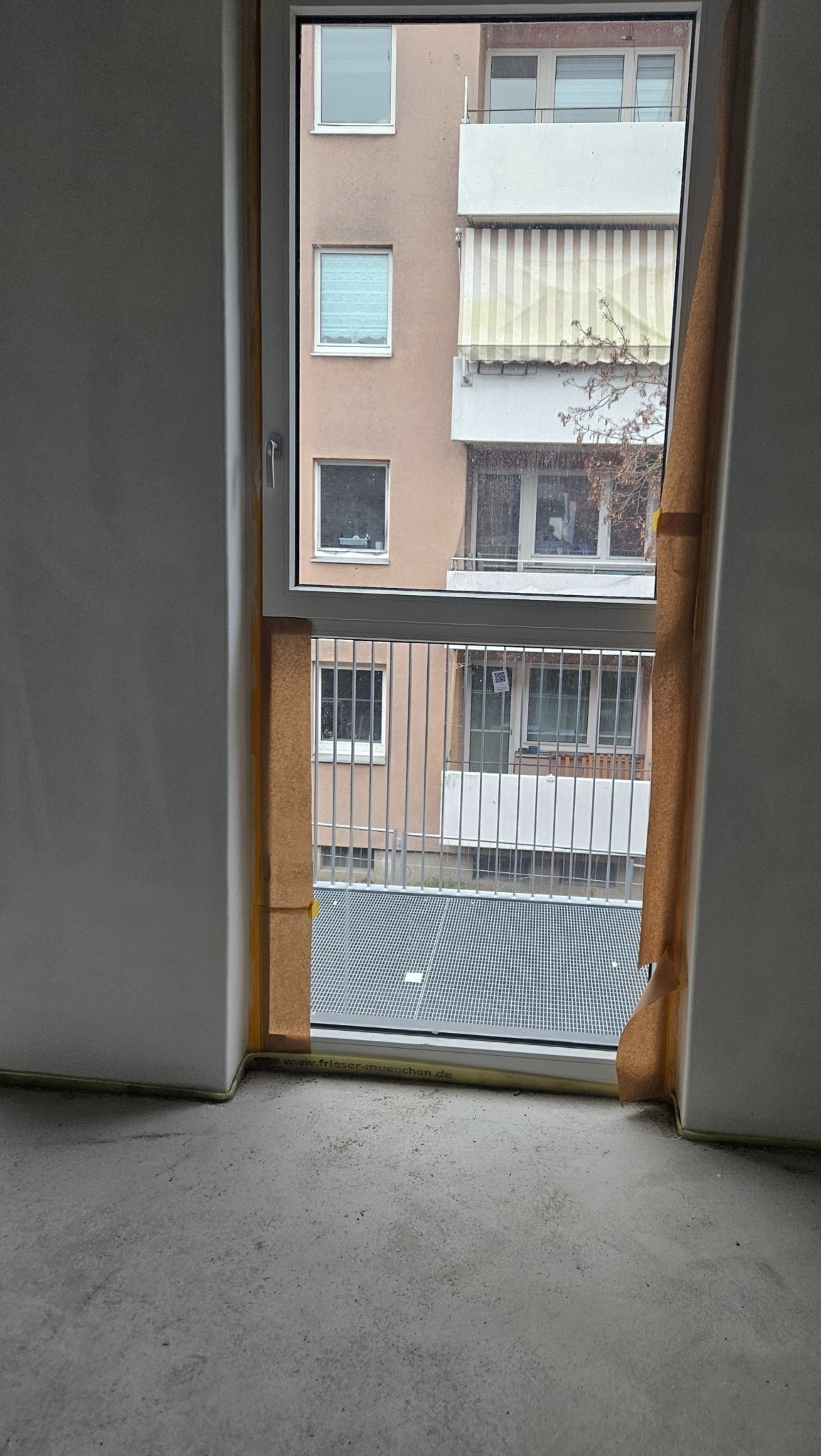 Nowo zamontowane okno, zabezpieczone taśmą malarską, widok na balkon z kratą w budynku wielorodzinnym