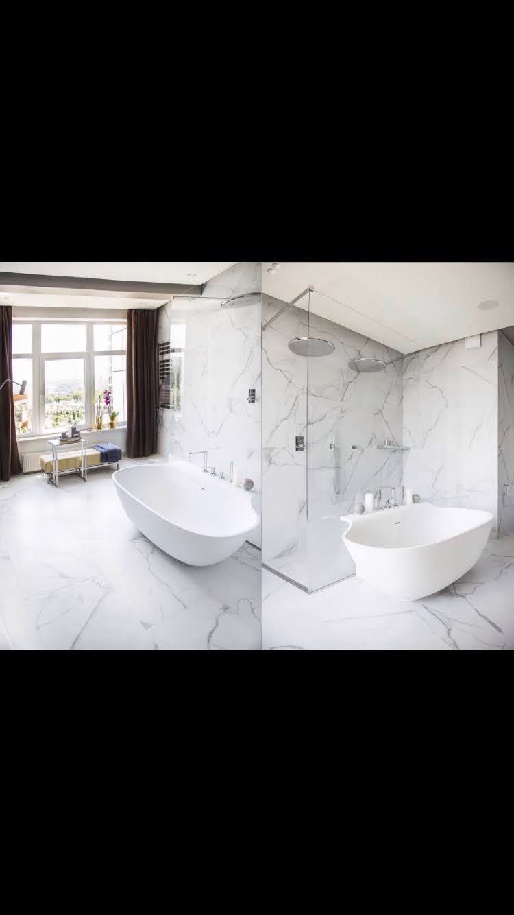 Nowoczesna łazienka z wolnostojącą wanną, kabiną prysznicową typu walk-in, marmurowymi płytkami na ścianach i podłodze, oraz oknem z ciemnymi zasłonami.