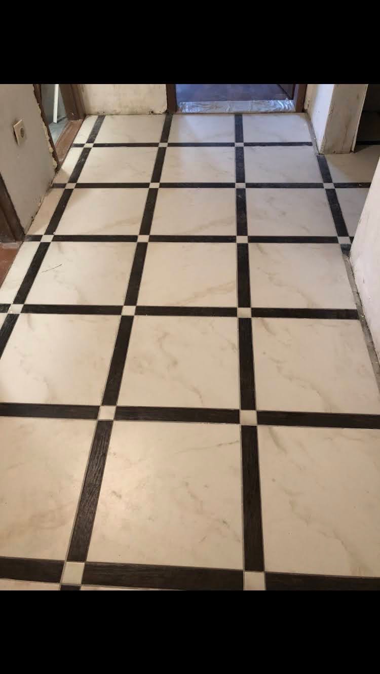 Wykończona podłoga w korytarzu z białych płytek imitujących marmur, przeciętych ciemnymi pasami płytek imitujących drewno, tworzącymi wzór szachownicy z małymi białymi kwadratami na skrzyżowaniach.