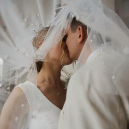 tojasun fotografia Sandra Stefańska - Pocałunek pary młodej pod welonem z perłami, w tle kolumnada. Romantyczne ujęcie z sesji ślubnej, delikatne światło podkreśla intymność chwili.