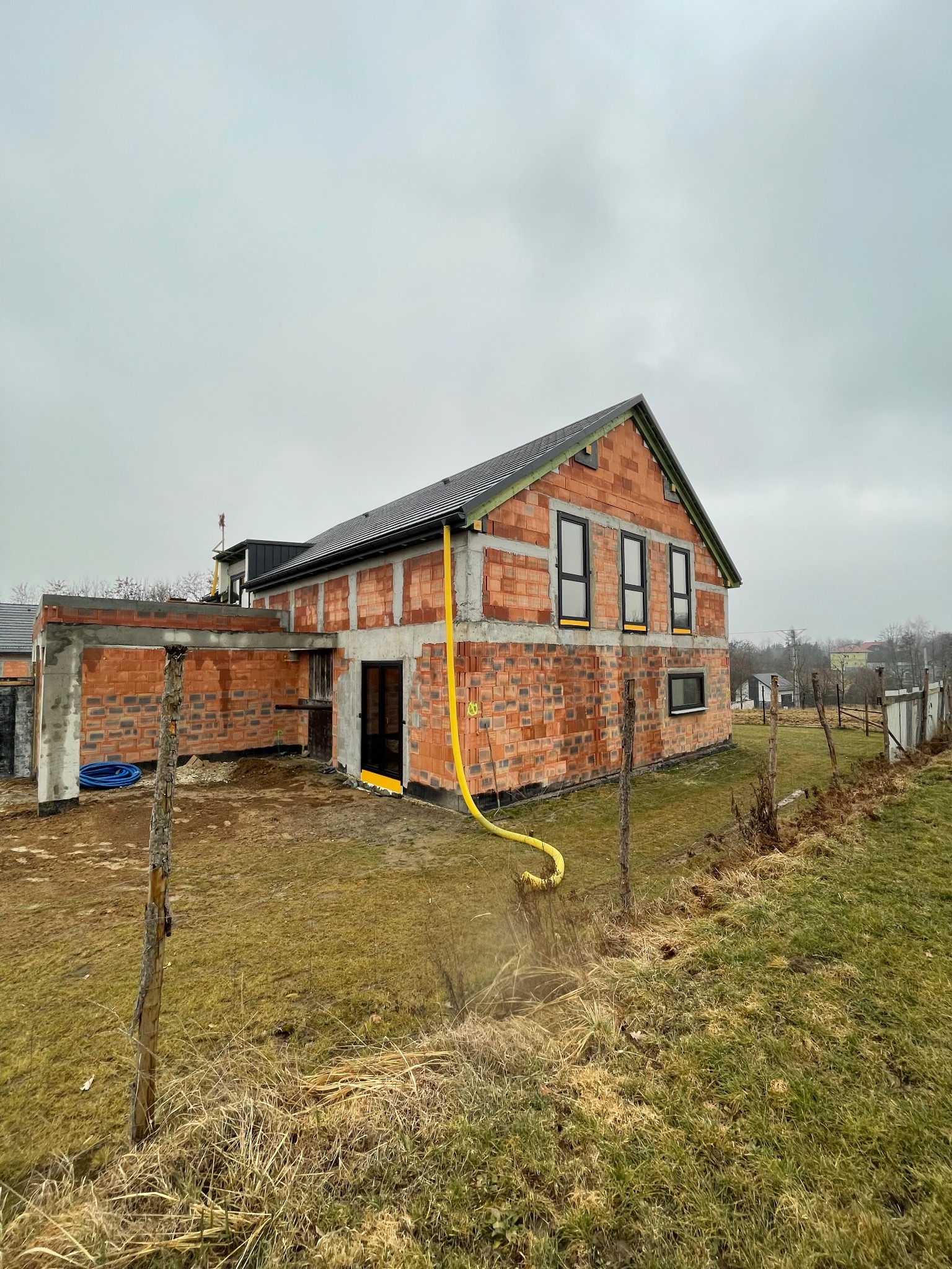 Budowa domu jednorodzinnego z oknami w czarnych ramach, widoczna instalacja żółtego węża doprowadzającego wodę.
