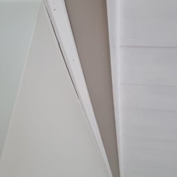 Przemysław Mazurek - Fragment pomalowanego wnętrza z widocznym połączeniem ściany w kolorze beżowym i białego sufitu panelowego, wykończonego białą listwą.