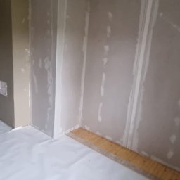 Przemysław Mazurek - Pokój w trakcie prac, ściany pokryte płytami kartonowo-gipsowymi, widoczne łączenia płyt, podłoga zabezpieczona folią malarską, listwa przypodłogowa częściowo zdjęta.