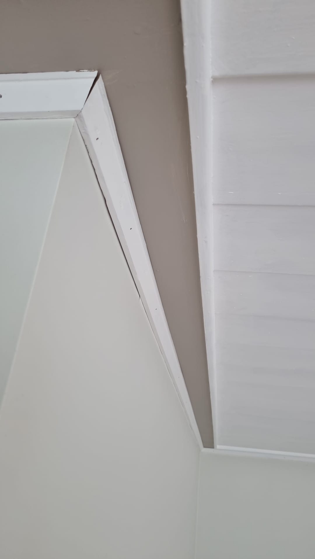 Fragment pomalowanego wnętrza z widocznym połączeniem ściany w kolorze beżowym i białego sufitu panelowego, wykończonego białą listwą.