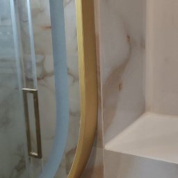 TL TARAS LITSEVYCH - Fragment łazienki z marmurową okładziną ściany, okrągłym lustrem w złotej ramie i białym gniazdkiem elektrycznym z wykończeniem w kolorze złota.