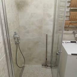 TL TARAS LITSEVYCH - Nowoczesna kabina prysznicowa z deszczownicą, wykończona beżowymi płytkami imitującymi marmur i mozaiką heksagonalną na podłodze, widoczna pralka i grzejnik drabinkowy.