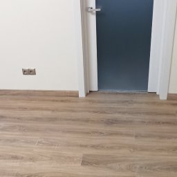 TL TARAS LITSEVYCH - Ułożone panele podłogowe w jasnym odcieniu drewna, widoczne dwie pary drzwi z ościeżnicami, gniazdka elektryczne na ścianie, listwy przypodłogowe w kolorze podłogi.