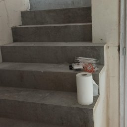 TL TARAS LITSEVYCH - Schody wykończone szarym kamieniem lub płytkami, z widocznymi narzędziami i materiałami budowlanymi, takimi jak szpachelka i rolka papieru, ściany w trakcie prac wykończeniowych.