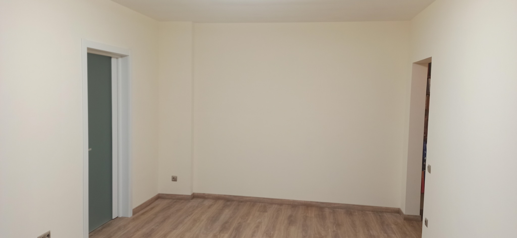Pusty pokój po remoncie z drewnopodobnymi panelami podłogowymi, świeżo pomalowanymi ścianami w odcieniu beżu oraz zamontowanymi drzwiami z mleczną szybą.