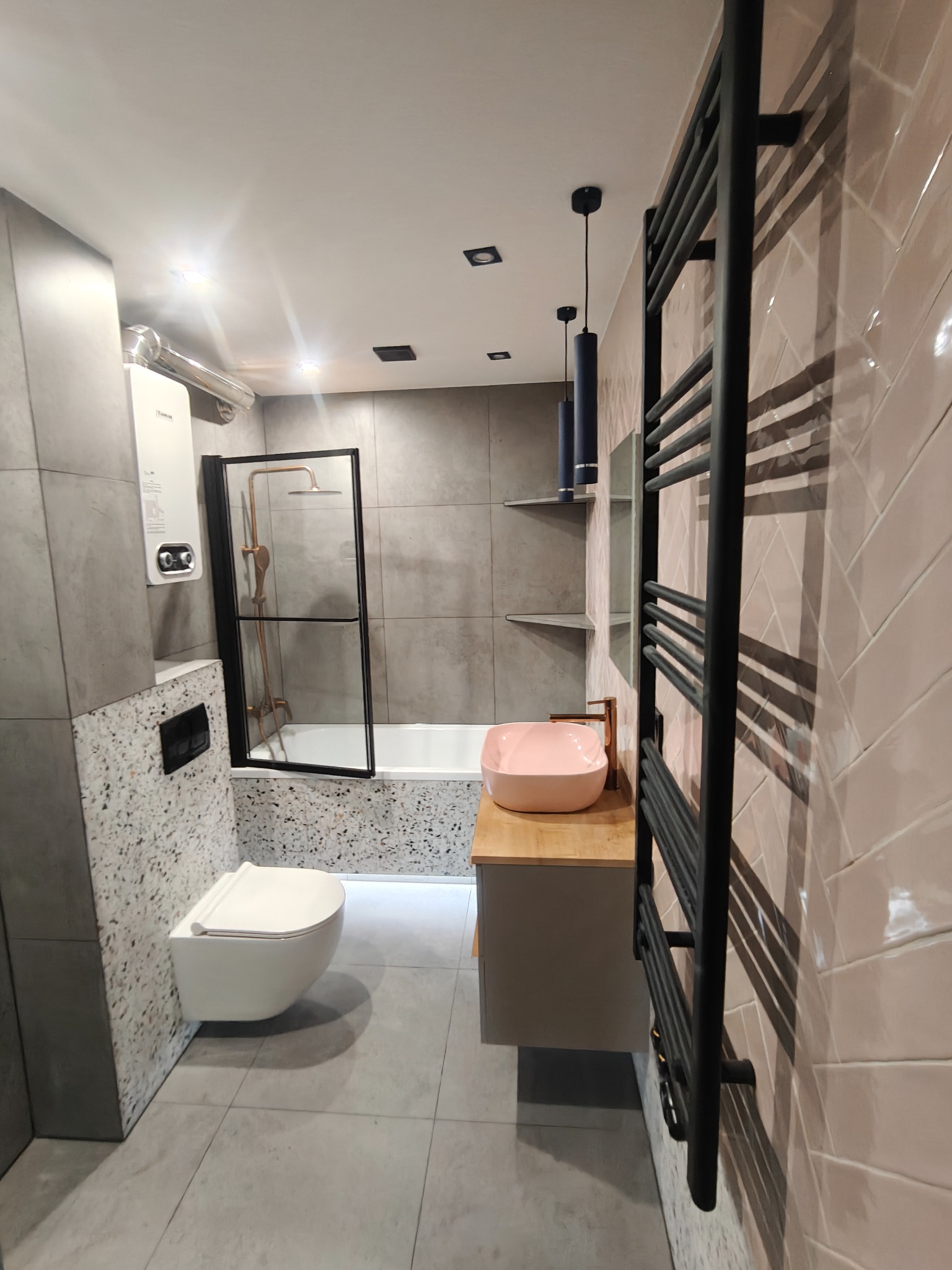 Nowoczesna łazienka po remoncie: różowa umywalka, czarny grzejnik drabinkowy, płytki w jodełkę i szare płytki wielkoformatowe. Minimalistyczny design i eleganckie wykończenie.