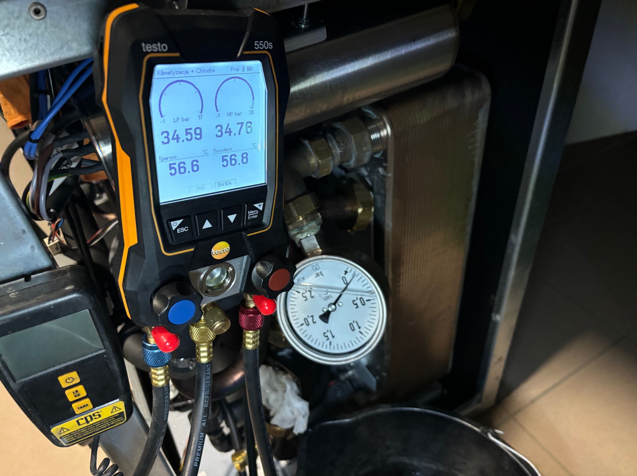 Pomiar ciśnienia i temperatury w instalacji chłodniczej za pomocą elektronicznego kolektora Testo 550s i manometru analogowego, widoczne przewody i elementy instalacji.