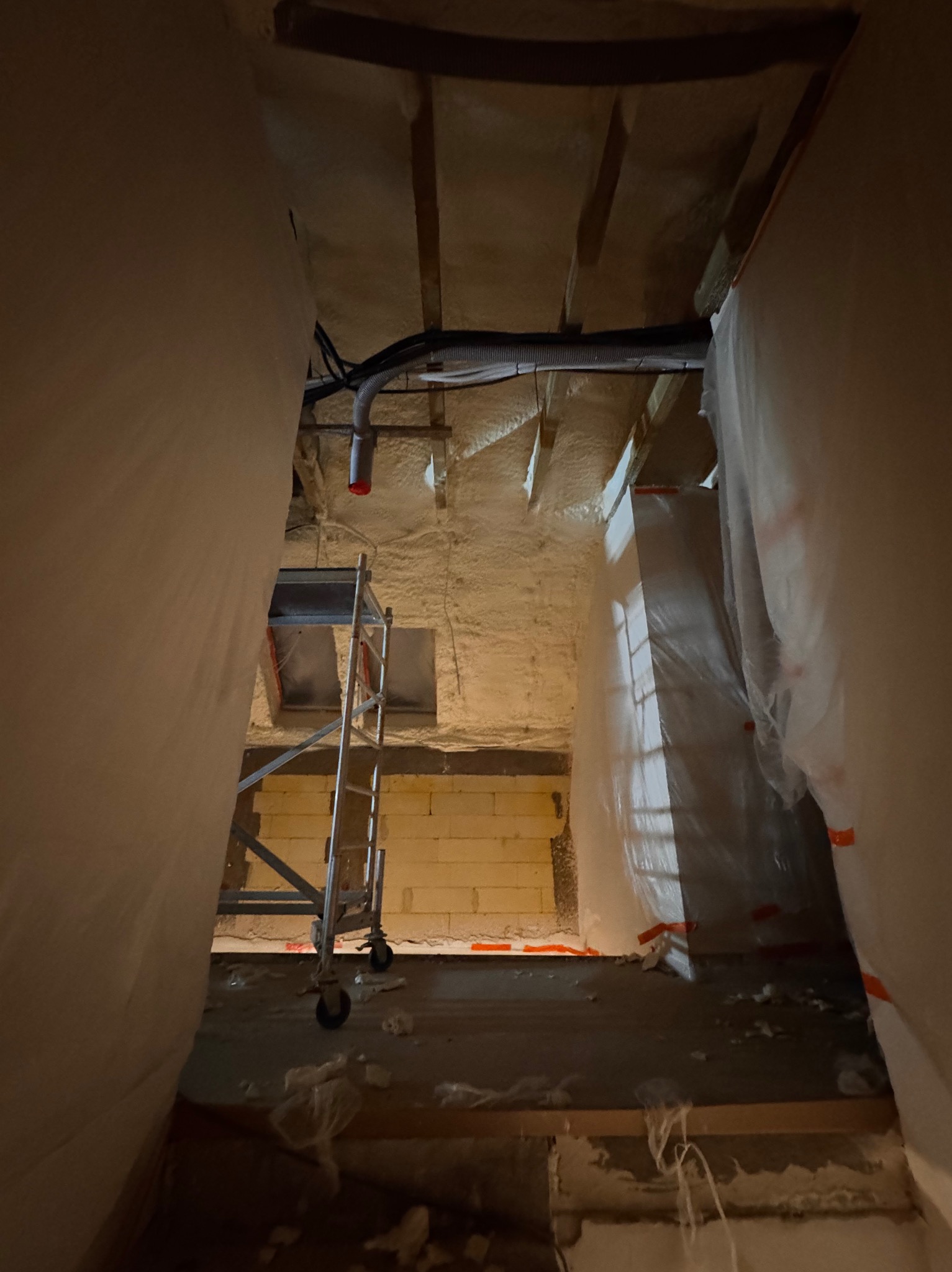 Poddasze w trakcie izolacji pianą PUR, widoczny fragment ściany z bloczków, rusztowanie i instalacja wentylacyjna pod sufitem.