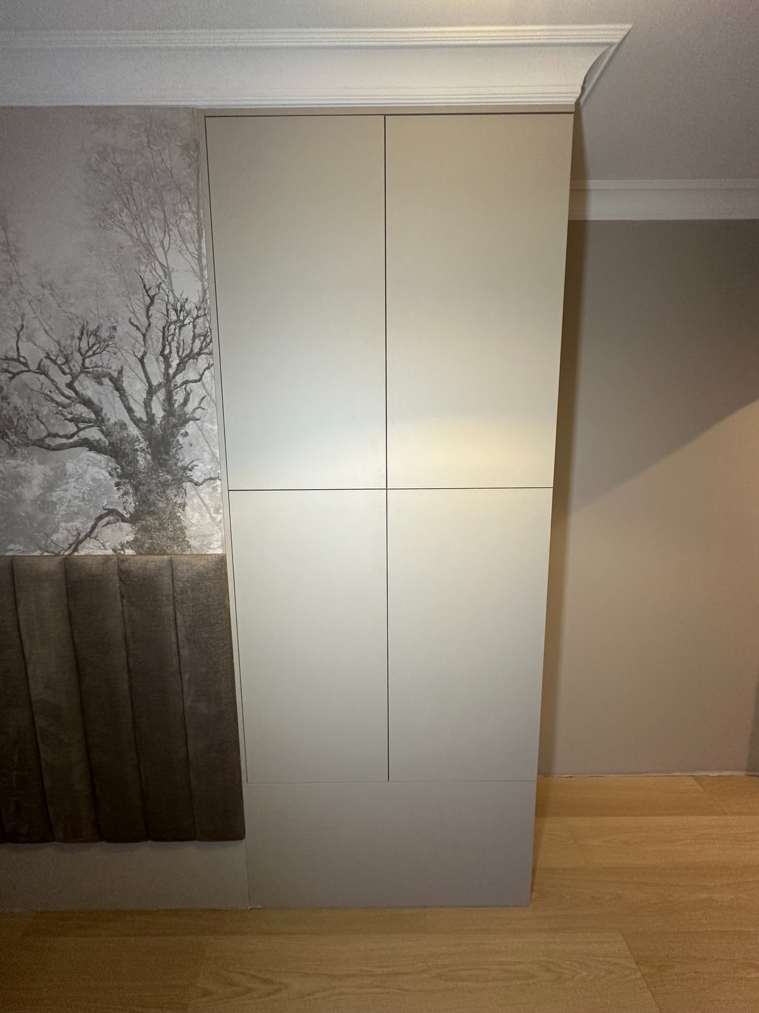 Biała szafa wnękowa z czterema drzwiami, wkomponowana w ścianę z tapetą z motywem drzewa i wezgłowiem łóżka w kolorze brązowym.