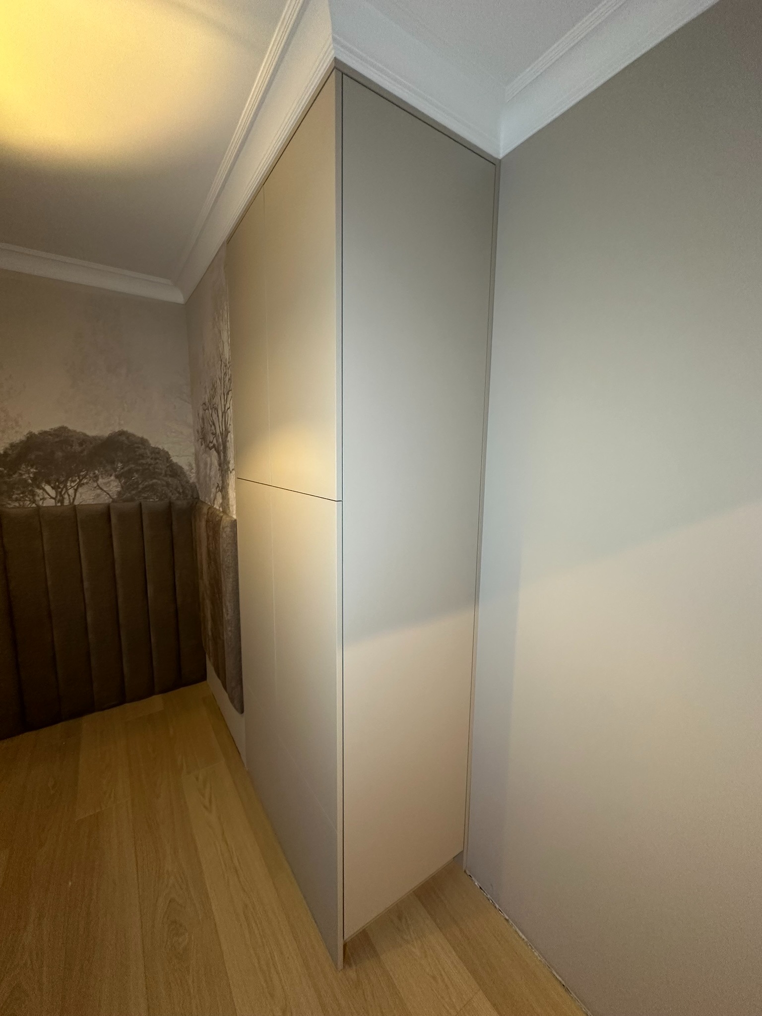 Szara szafa wnękowa z przesuwnymi drzwiami, dopasowana do wnętrza sypialni z tapetą z motywem drzewa i wezgłowiem łóżka w kolorze brązowym.