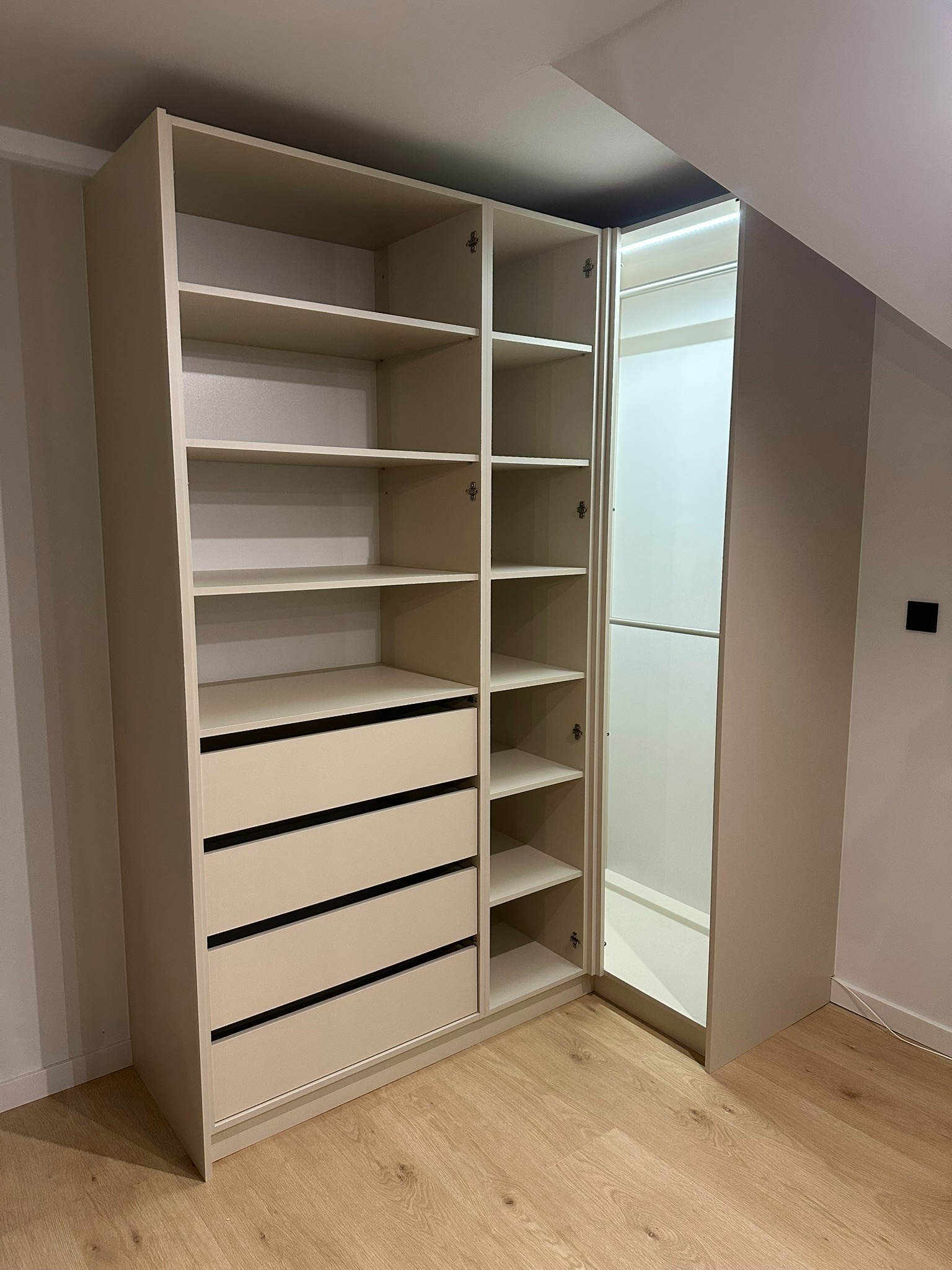 Jasna, narożna garderoba z szufladami i półkami, z oświetleniem LED wewnątrz, zamontowana na poddaszu ze skośnym sufitem.