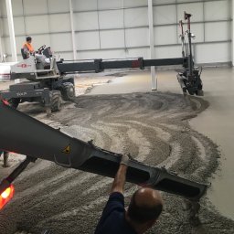 SDI - Wylewka posadzki przemysłowej w hali: operator na maszynie Mega Floor SXP rozprowadza beton, drugi pracownik kontroluje proces z bliska. Widoczne świeże i gładkie fragmenty.