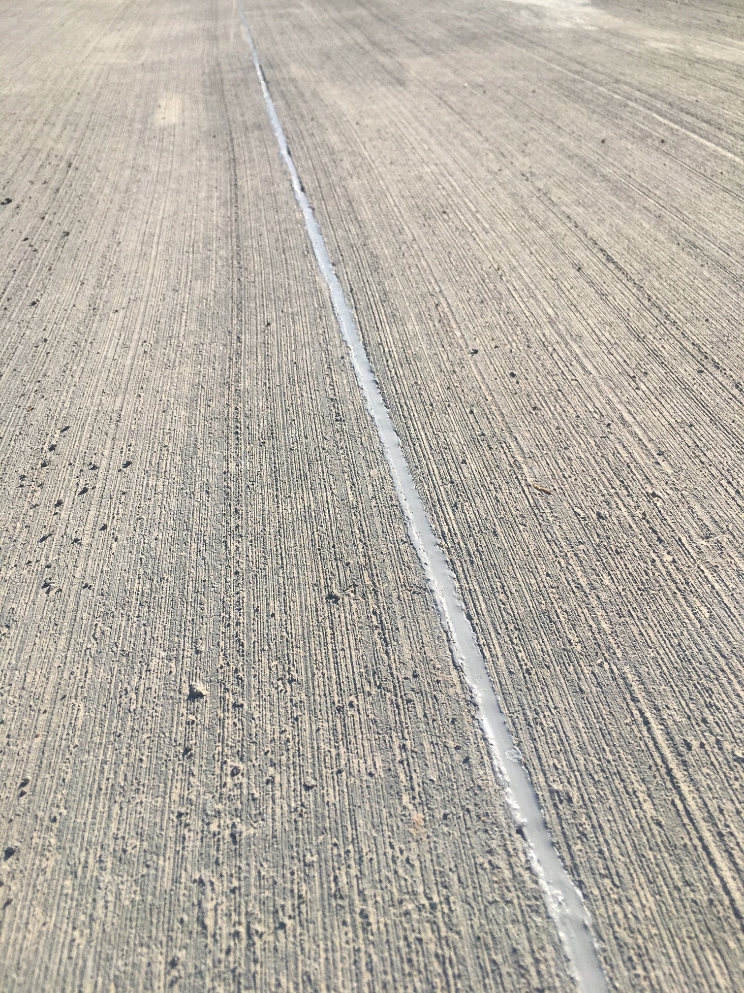 Szlifowana, jasnoszara powierzchnia betonowa z wyraźną szczeliną dylatacyjną wypełnioną szarą masą uszczelniającą, widziana pod kątem.