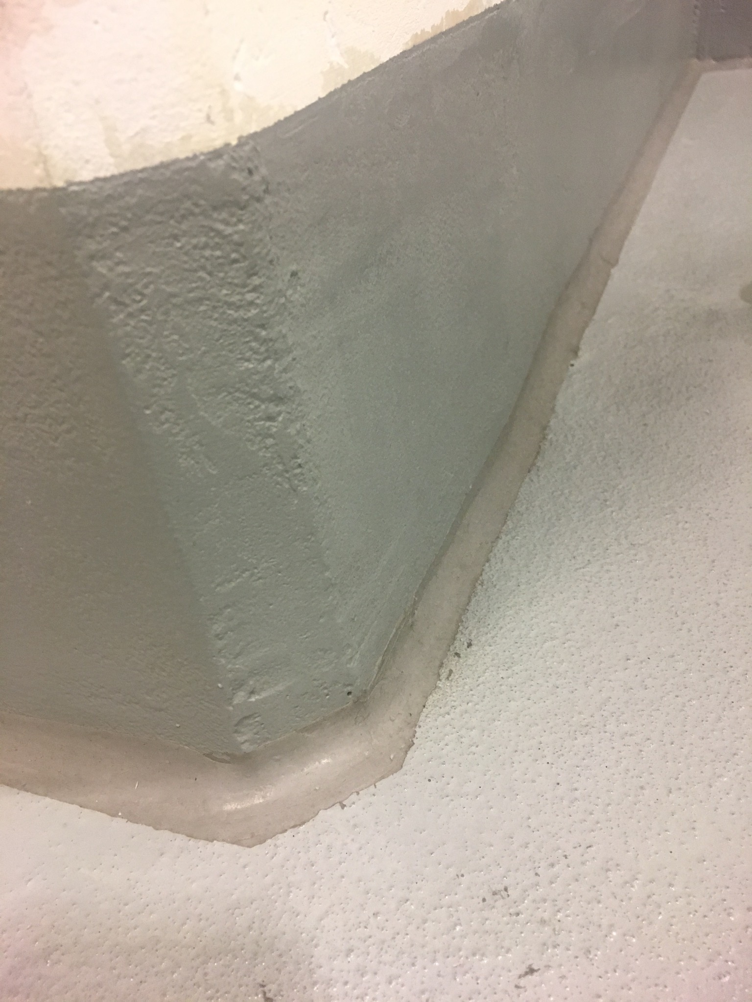 Szara, gładka posadzka żywiczna z wykończeniem przy ścianie, widoczne drobne nierówności i struktura powierzchni. Kąt ujęcia podkreśla perspektywę pomieszczenia.