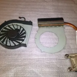 Zdemontowany układ chłodzenia laptopa: wentylator z czarną obudową i radiatorem z miedzianą rurką cieplną, obok leżą śrubokręty na folii bąbelkowej.